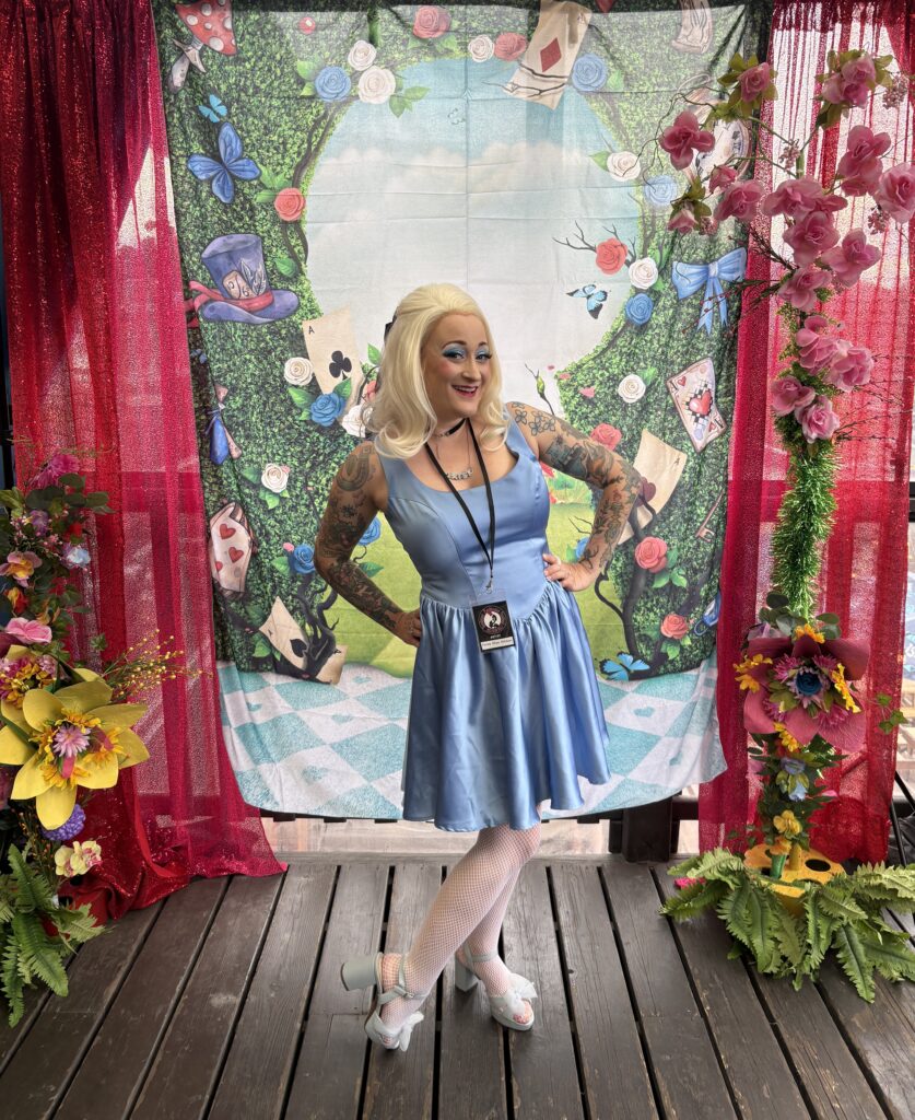 blonde posing in a blue dress in front of an Alice in Wonderland backdrop